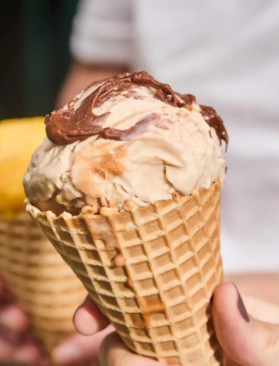 Cono de gelato de avellanas con chocolate derretido por encima, sostenido en una mano