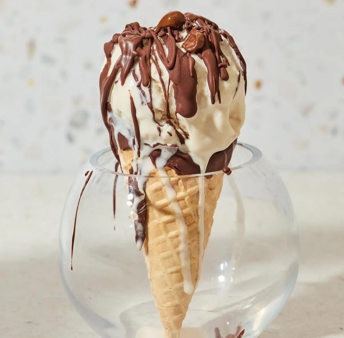 Cono de gelato stracciatella bañado en chocolate derretido, servido en una copa de vidrio