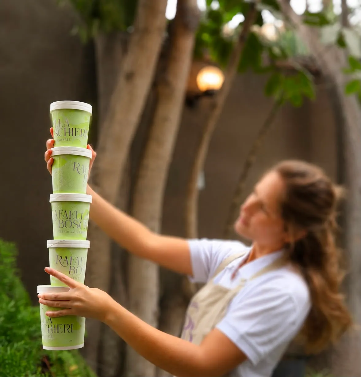 Una persona sosteniendo una torre de potes de gelato de pistacho al aire libre