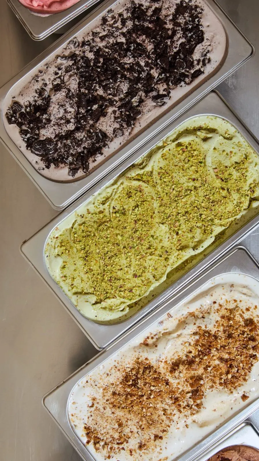 Vista superior de tinas de gelato recién preparadas: cookies and cream, pistacho y avellana con nutella